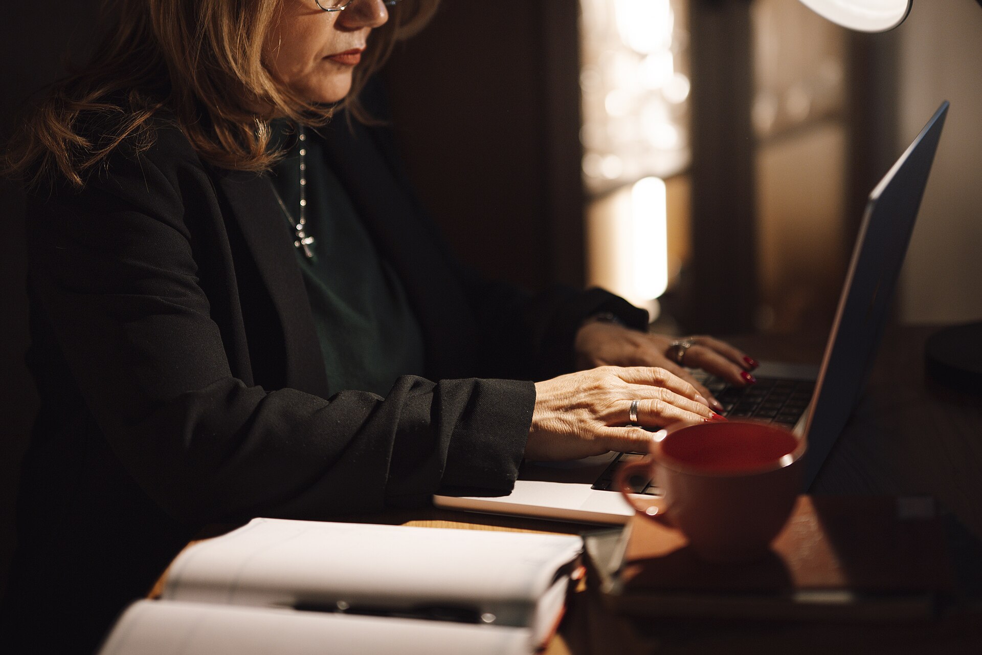 A freelancer working on a laptop in a home office with a coffee and notebooks.